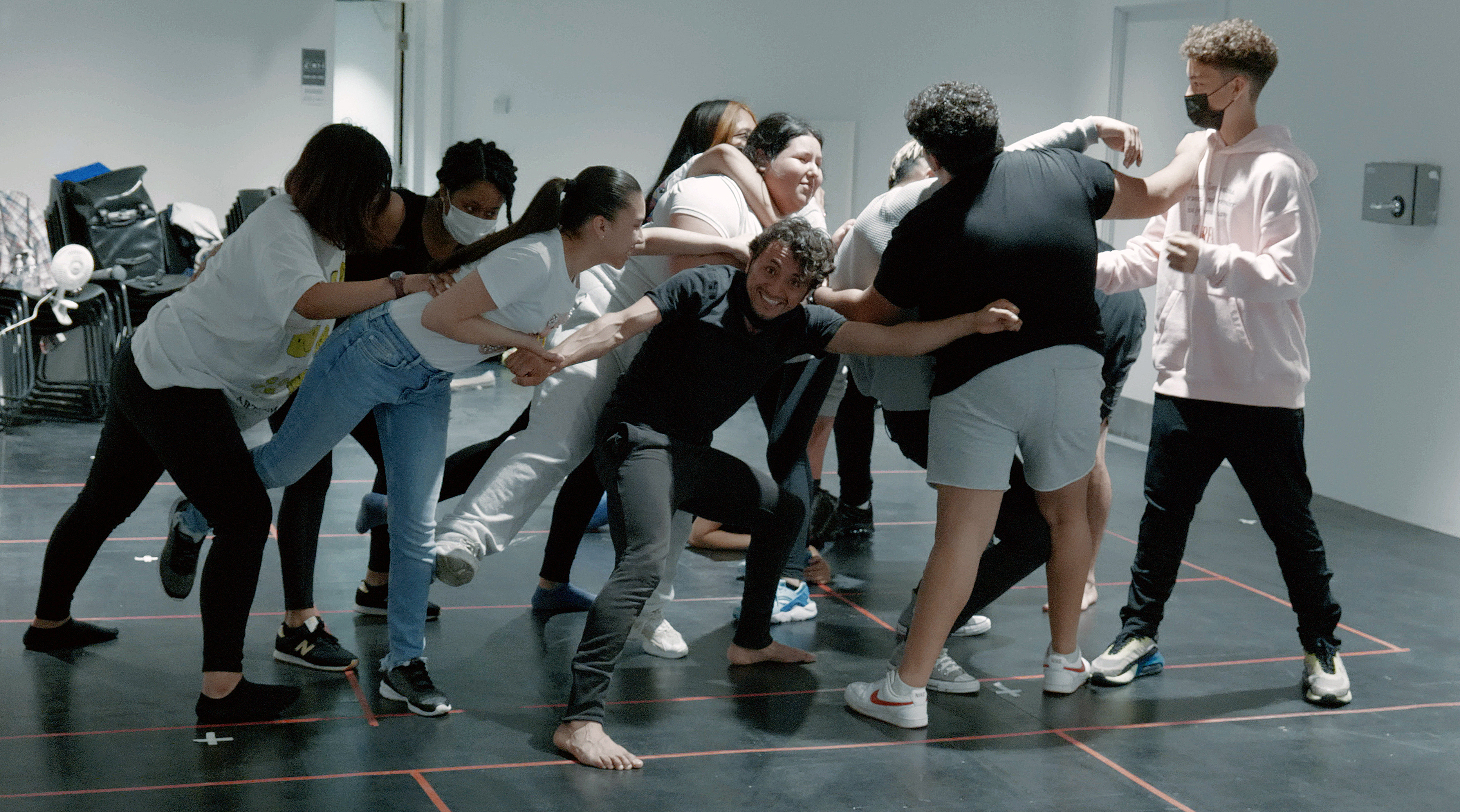 group of young people in a rehearsal room all physically connected and moving 